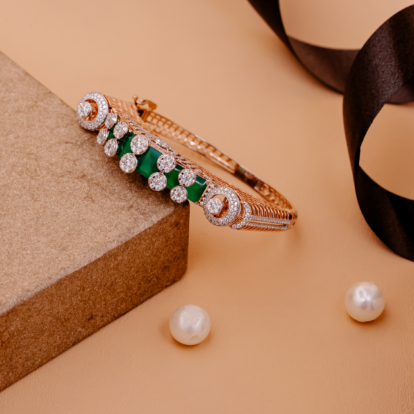 Elegant gold bangle with green gemstone accents and halo-set crystals on a beige background.