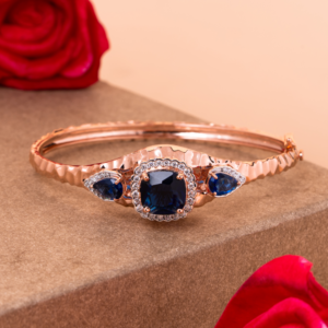 Luxurious rose gold bangle adorned with deep blue sapphire gemstones surrounded by sparkling diamonds, designed to resemble a regal crown with timeless elegance